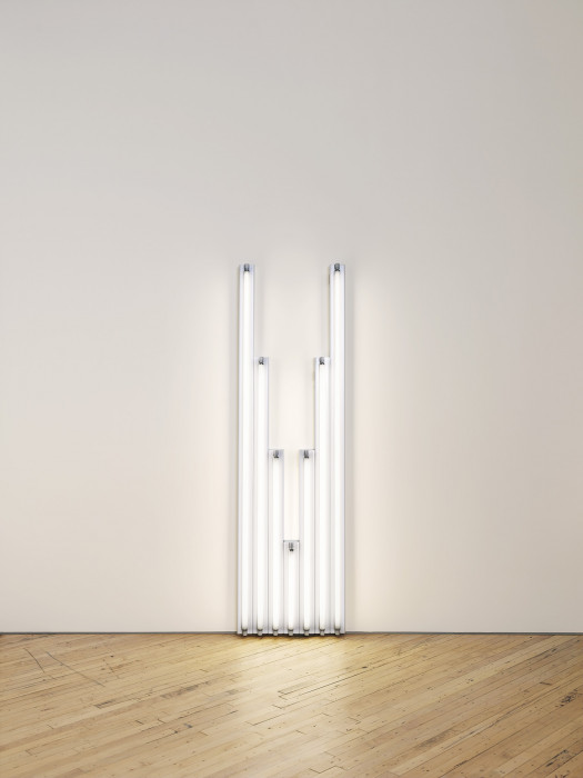 Seven fluorescent-white, tubular lights positioned against a white wall, four of which are arranged in descending order from tallest to shortest, shortest light at center is followed by three more lights arranged in ascending order from shortest to tallest.