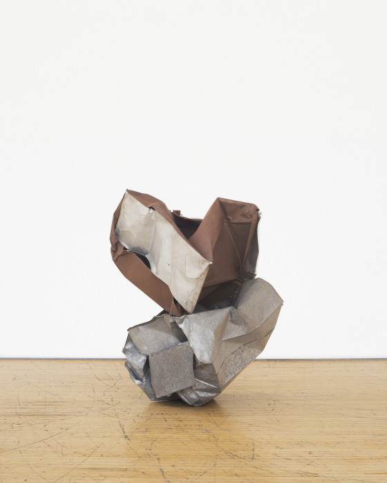 A sculpture made of brown and silver metal parts that twist together rests on a wooden floor.