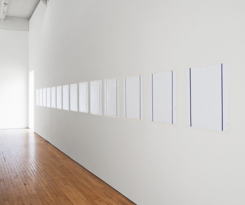 Angled view of a room where fourteen evenly spaced white squares are hung from a white wall. Two blue lines run vertically near the edges of each square.