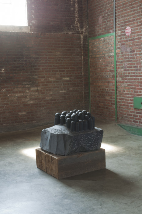 A dark sculpture with domed cylinders sprouting from its base on top of a solid slab of wood.