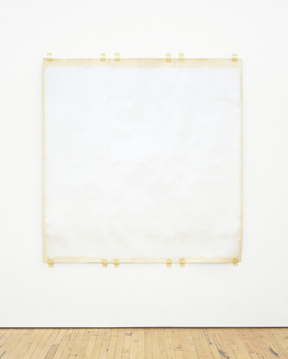 A square sheet of cream-colored paper painted off-white is taped to a white wall at the top and bottom edges. The edges are unpainted.