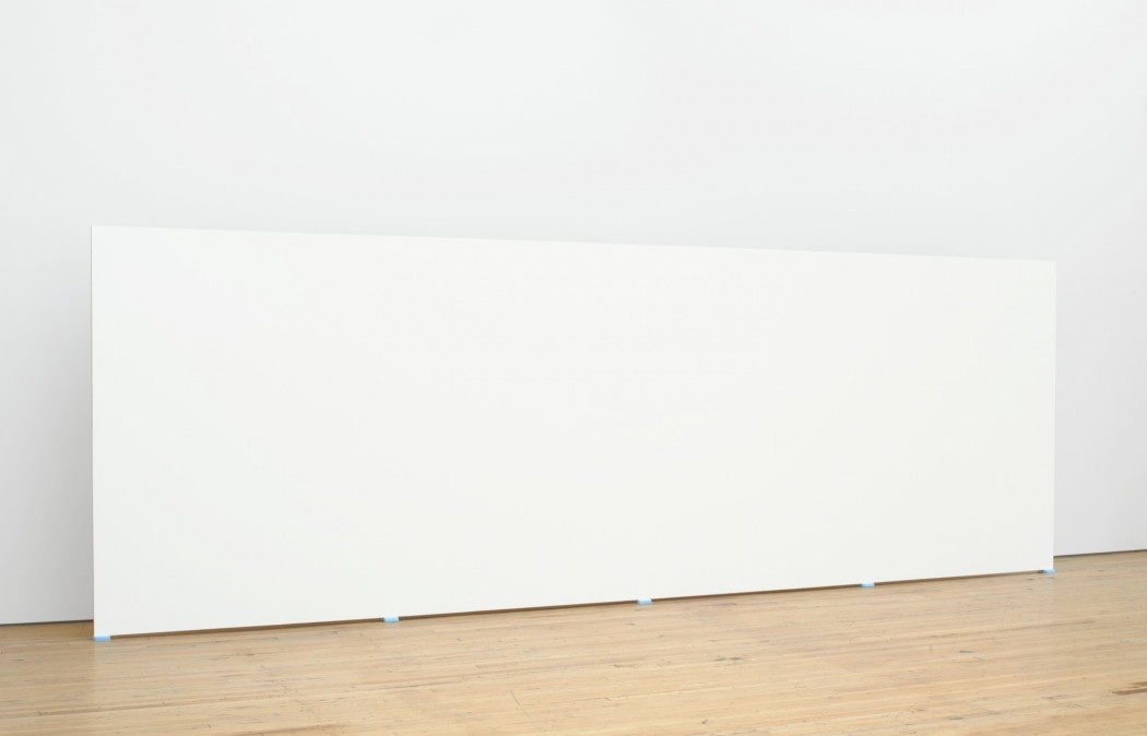 A long, white, rectangular form is propped above a floor with five small, blue, foam blocks.
