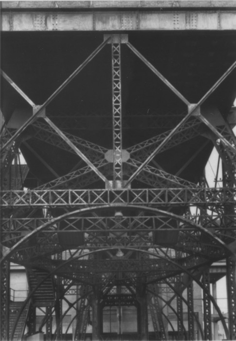 Black-and-white photograph of metallic vertical, diagonal, and horizontal trusses and arches across a space.