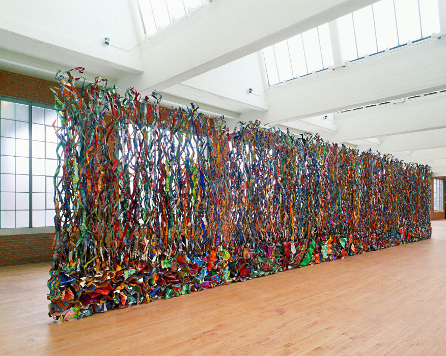 Freestanding tall curtain-like sculpture composed of multicolored thin, twisting vertical metal strips.