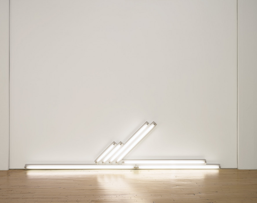 Several white fluorescent tubes sit on the floor and others are mounted horizontally on the wall.
