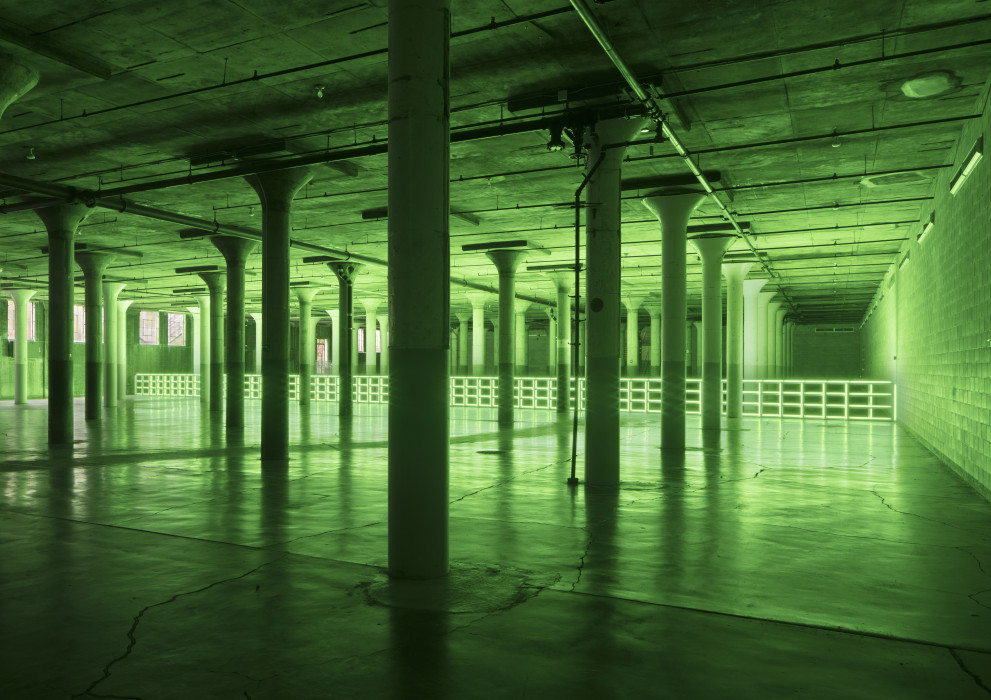 A green fluorescent barrier spans a large dark room with pillars.