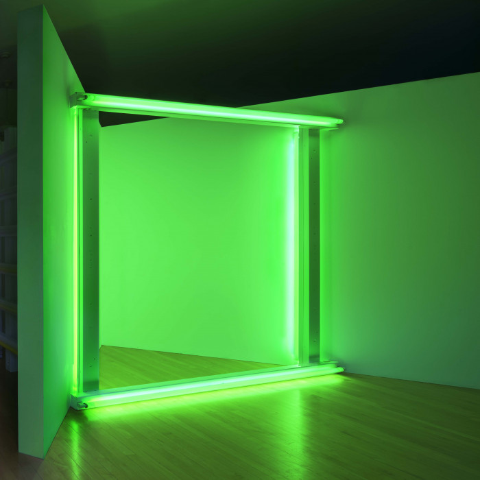 Four green florescent lightbulbs, configured into a square and situated in a corner, casting a green wash of light.