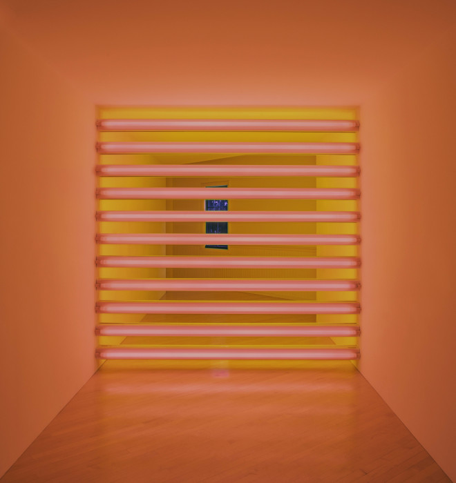 A grid of eleven horizontally oriented, tube-shaped, flourescent bulbs emit a pink light in the foreground and a yellow light in the background of a room.