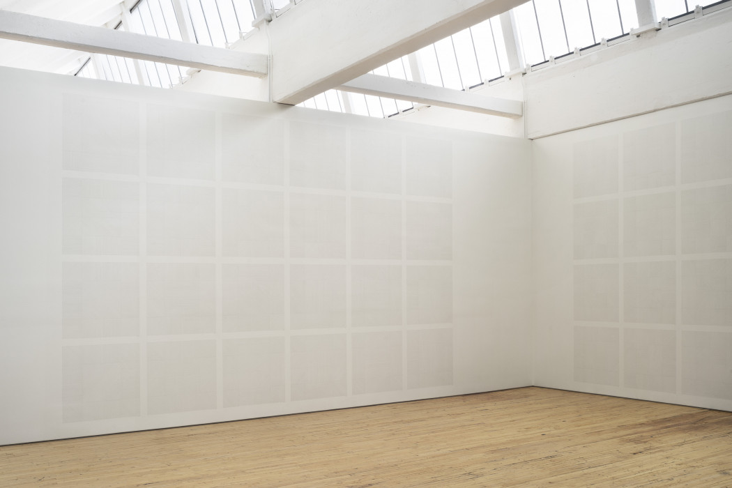 A grid of white drawings cover the space of two white walls. 