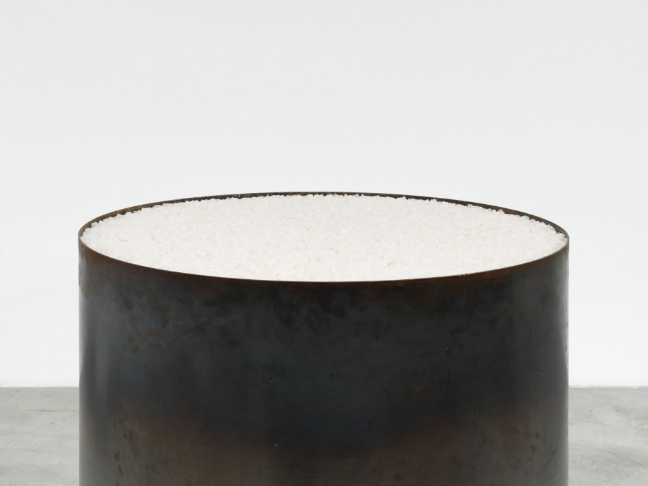 A close up shot of the opening top of a large steel tube-shaped vessel containing large chunks of salt. The steel is vary dark and dull, with various marks and smudges.