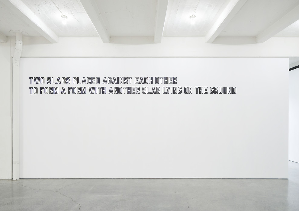 White text outlined in black is placed high on a white wall. The text reads: 