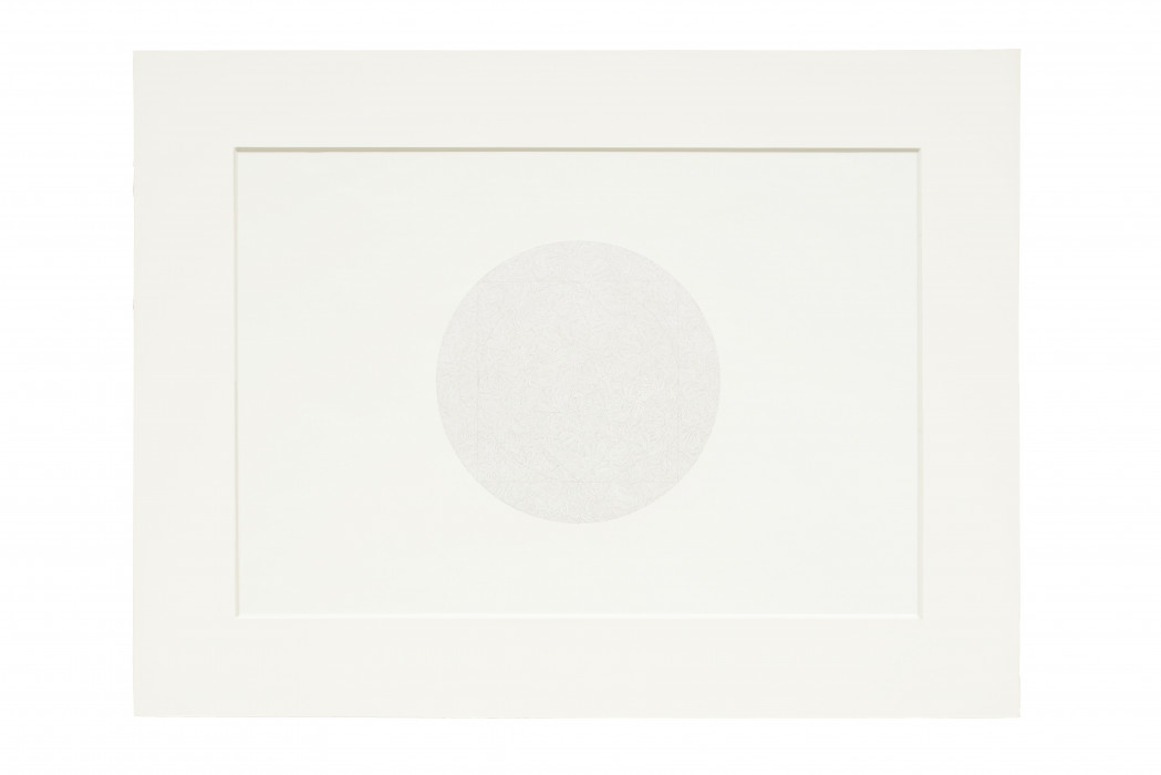 An horizontally oriented, white rectangular sheet of paper features a faint circular drawing of curvilinear lines at center and is placed on a white matte board.
