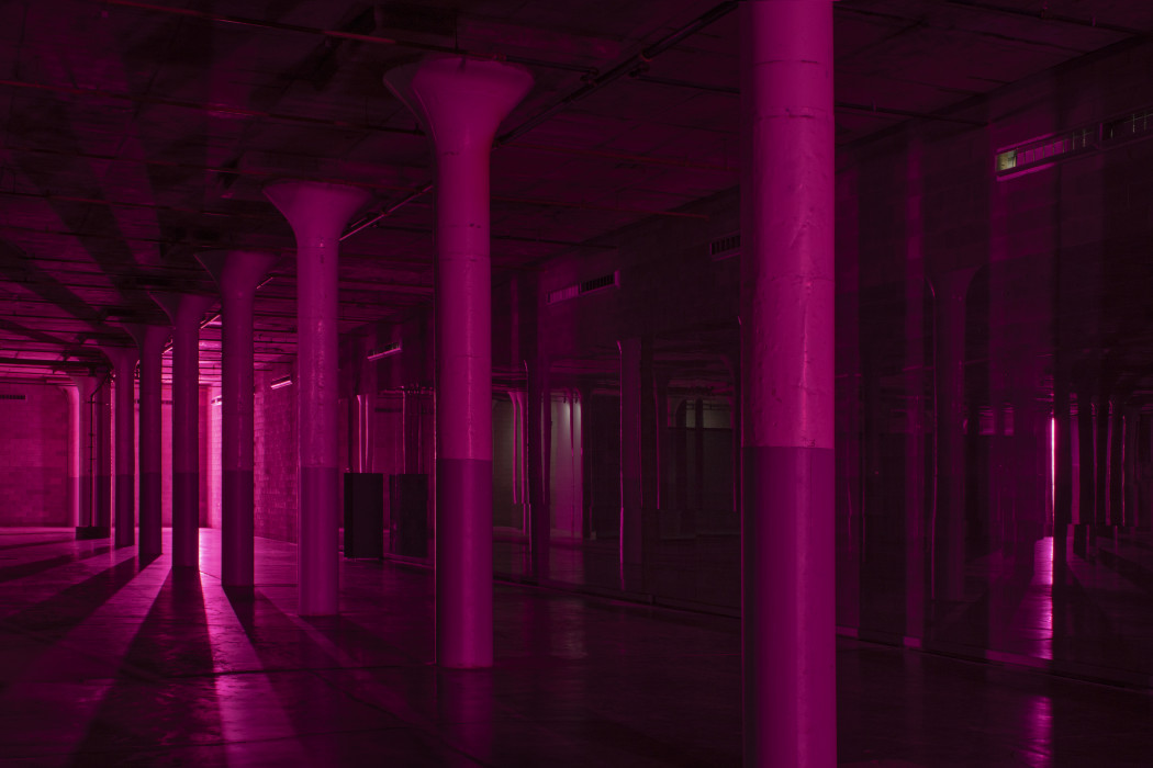 A dark industrial basement with a row of cement columns is backlit in magenta.