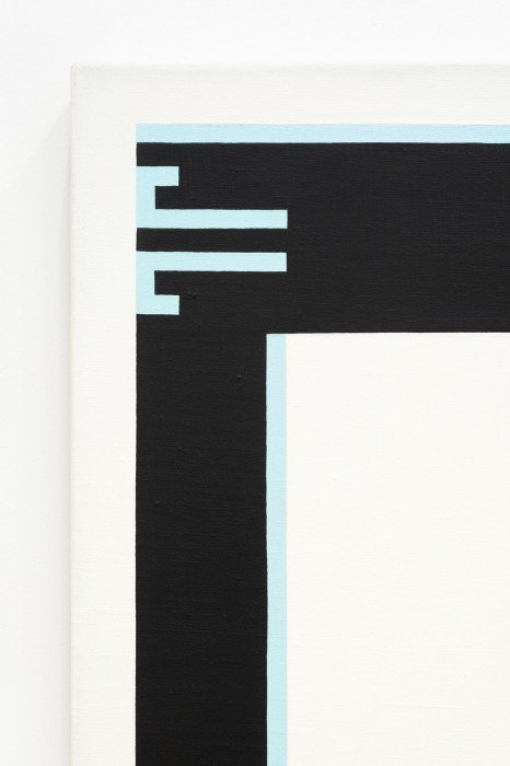 A detail of the upper left corner of a white canvas on a white wall. The top and left corner of a black border within the white canvas is shown, along with light blue lines at the upper left corner of the black corner.