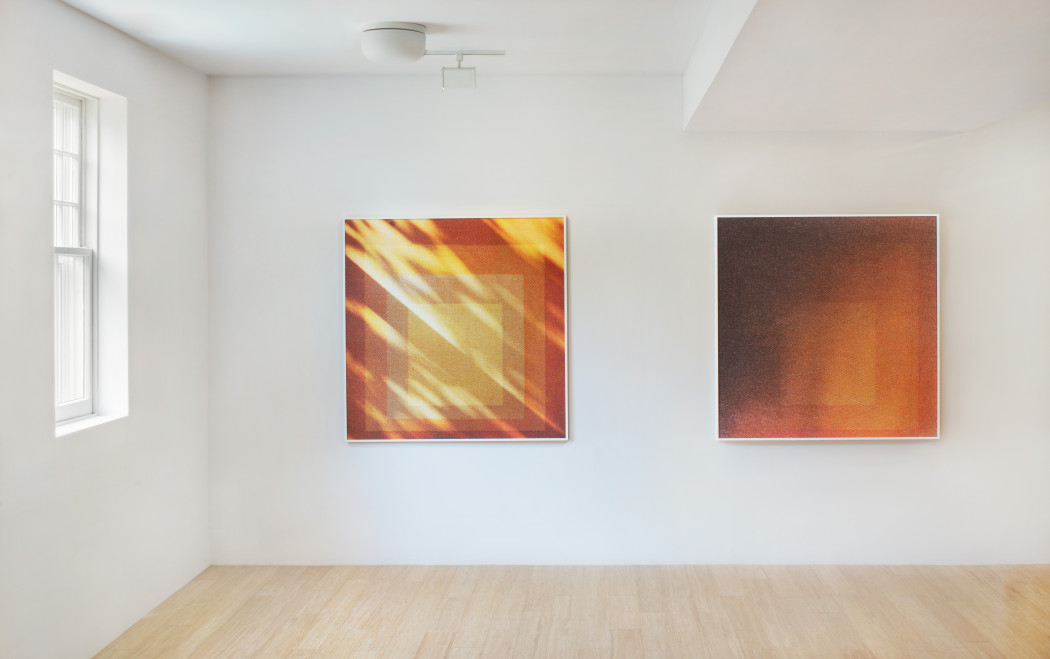 Two warm-colored square paintings hang on a white wall, both with orange hues and concentric square shapes. The left looks as if it were being flooded by sunlight through something like trees.