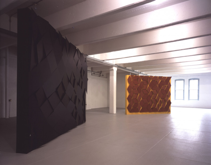 Two large rectangular sculptures with 3D geometric patterns on them stand in an industrial space.