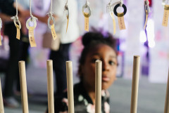 A girl gazes up at a group of name-labeled washers hung by white string above wooden dowels in the foreground.