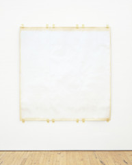 A square sheet of cream-colored paper painted off-white is taped to a white wall at the top and bottom edges. The edges are unpainted.