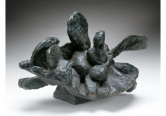 An irregular bronze form with several oddly shaped protuberances rests on a white surface.