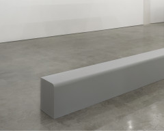 A long gray beam lies on a cement floor.