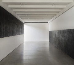 Two parallel walls are painted half black and half white, with black above white on the left wall, and white above black on the right wall, both extending toward but not conjoined by a perpendicular white wall.