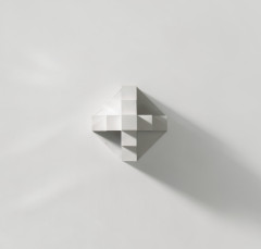 A protruding, white geometric cross mounted on a white wall with a shadow casting on the bottom right side of the cross. The cross is made up of three levels of cubes that increase to the intersection of the cross.