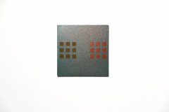 Two sets of three-by-three evenly spaced squares are on opposite sides of the artwork, against an iridescent blue glitter background. The left set of squares are iridescent ochre and the right set of squares are iridescent red.