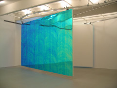 A large divider of reflective, iridescent blue panels hangs from a ceiling track in the middle of a white room.