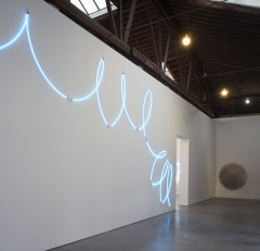 A thin, neon blue looping line runs along the length of a white wall.