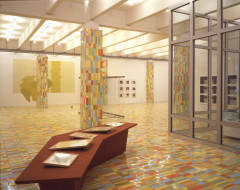 Multicolored mosiaced floor and columns in a gallery space with artworks on the walls and in the space.