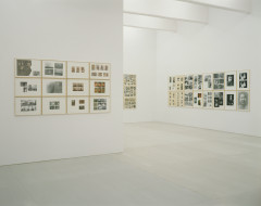 Mutliple framed gridded images hang on multiple white gallery walls.