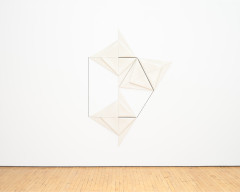 A geometric artwork featuring folded, triangular pieces hangs on a white wall.