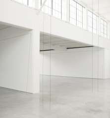 Two pairs of thin black lines stretch from a cement floor to a white celing in a large white room filled with natural light. Two thin green outlines of rectanglar shapes rest against white walls of two adjoining rooms.