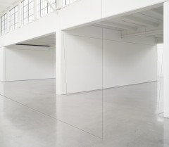 A thin black line rests on a cement floor and meets another thin black line that stretches toward the ceiling to form a right angle in a large white room filled with natural light. Two thin green outlines of rectanglar shapes rest against white walls of two adjoining rooms.