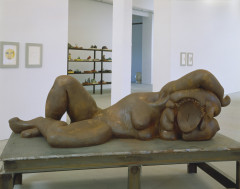 A large metal sculpture of a humanoid figure with no face reclining on a metal table.