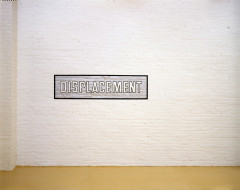 A white brick wall with a silver rectangle with a black border painted onto it, and the word 