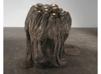 An irregularly shaped, bronze sculpture with circular structures coming out of its base is placed on a cement floor.
