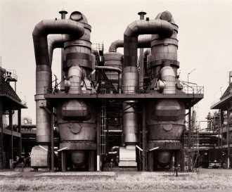 Black-and-white photograph of factory with curving cylindrical tubes, tanks, and other protuberances