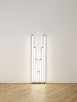 Seven fluorescent-white, tubular lights positioned against a white wall, four of which are arranged in descending order from tallest to shortest, shortest light at center is followed by three more lights arranged in ascending order from shortest to tallest.