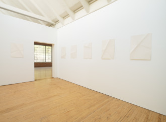 Six sheets of creased paper are evenly spaced along the horizon of two white walls and an open doorway.