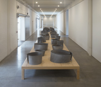 A low wooden table, on which many small, circular, metal shapes are placed in two rows, sits in a hallway.