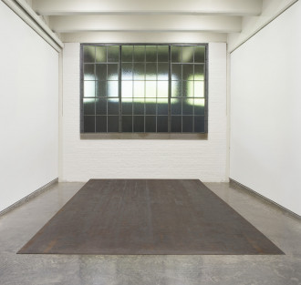 Room with window, white walls, and slightly slanted, steel slab resting on cement floor