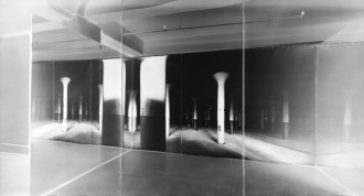 An inverted black and white photo of a large, long hanging print of evenly spaced columns in a large space.