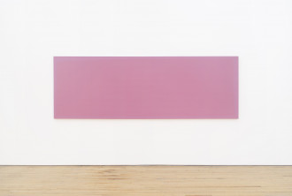 A long rectangular painting of medium pink with a lighter pink border hangs horizontally from a white wall above a wooden floor.