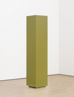 A tall, green column is placed on a wooden floor in front of two white walls.