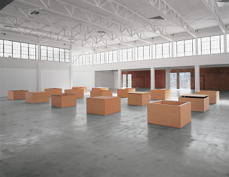 Five rows of three large plywood boxes sit on a concrete floor in a bright industrial space.