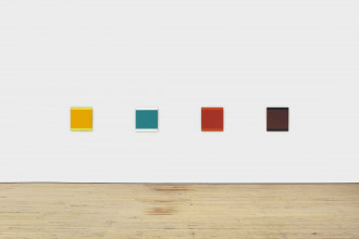 Four identically square-shaped, different color-blocked paintings of yellow, blue, red, and black hang on a white wall.