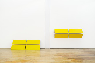 Two identical yellow, rectangular-gridded structures touch a white wall. The left structure sits on the groun and leans against the wall. The right structure hangs on the wall.