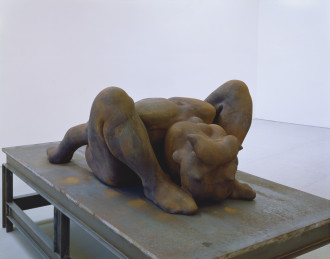 A large metal sculpture of a curled up humanoid figure sitting on a metal table.