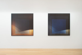 Two square paintings hang on a white wall, the left with dark and orange hues, the right one with dark and blue hues.. Both depict layered concentric squares with curved lightened areas coming from the bottom and lower left of each canvas.